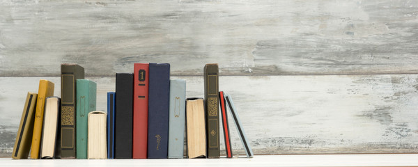 Composition with vintage old hardback books, diary, fanned pages on wooden deck table and abstract...