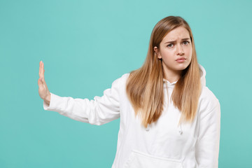 Concerned young woman girl in casual white hoodie posing isolated on blue turquoise wall background studio portrait. People lifestyle concept. Mock up copy space. Showing stop gesture with palm aside.