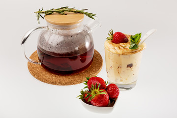 Fresh strawberries in a white saucer, a glass teapot and tiramisu in a glass glass