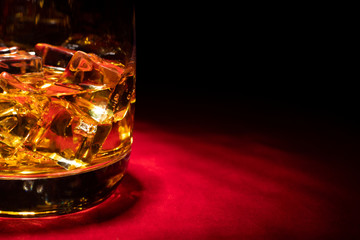 The bottom of a whisky glass with ice on the red table.