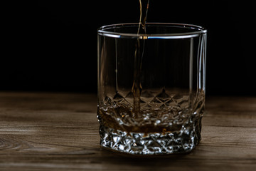 glass with a drink of dark color side view, splashes and foam from the drink. Selective focus