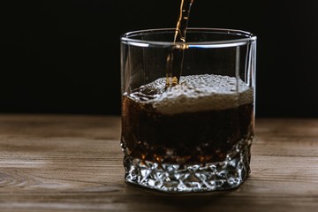 glass with a drink of dark color side view, splashes and foam from the drink. Selective focus