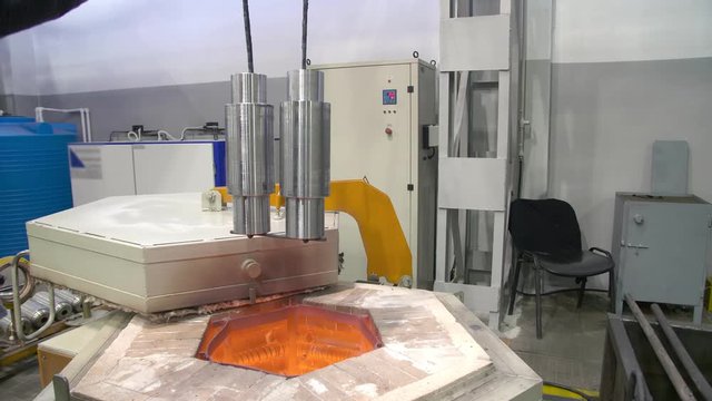 A worker uses a crane to lower metal parts into a quenching furnace. Quenching of steel billets. The metal shop. 4K