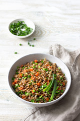 Delicious vegan buckwheat with vegetables and green onions on a light wooden background. Healthy homemade food