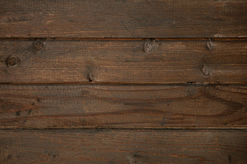 Dark brown surface of an old wooden floor, wall or table with cracks and knots. Dark rough weathered wood.