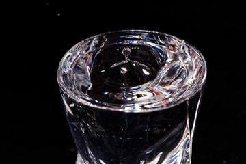 Black background is a glass in which a drop of water falls. Splashing water on glass
