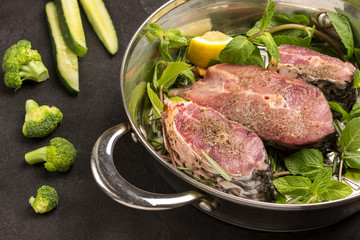 Chopped river fish with mint and rosemary in pan. Broccoli and sliced cucumbers on table