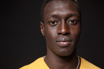 Close up of young african american man guy in yellow t-shirt posing isolated on black wall background studio portrait. People sincere emotions lifestyle concept. Mock up copy space. Looking camera.
