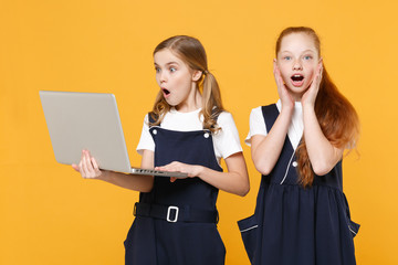Two girls 12-13 years old in white t-shirt blue school uniform hold laptop pc computer isolated on yellow background children studio portrait Childhood education lifestyle concept Mock up copy space