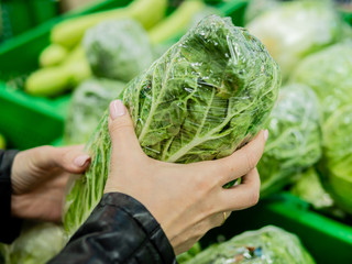 Female buyer chooses a cabbage in the supermarket. Close-up of female hands with Chinese cabbage.