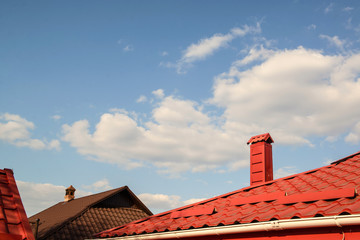 Red roof of a house on a blue sky with clouds