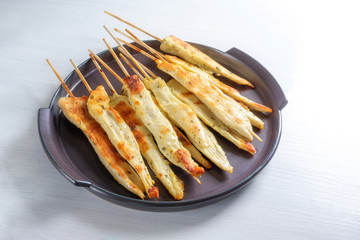 Roasted chicken skewers, Mediterranean finger food snack for a festive holiday party on a dark purple plate, white painted wooden table with copy space