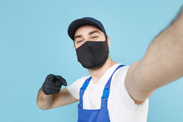 Delivery man in cap t-shirt coveralls uniform sterile face mask gloves isolated on blue background...