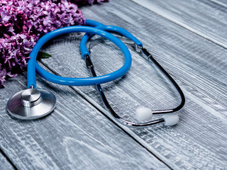 Stethoscope or phonendoscope on a wooden deck next to a bouquet of lilacs. Medical and healthcare concept