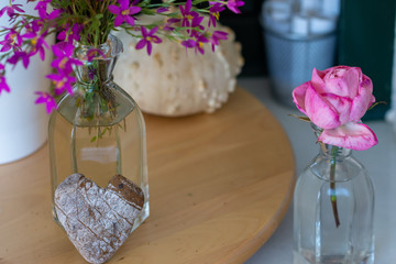 Interior decoration: home corner with a pink rose, a dried pumpkin, a glass vase with wild flowers and a heart-shaped stone