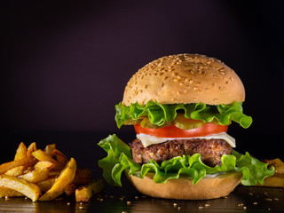 Hamburger with beef cutlet, tomato, pickles, lettuce, and cheese, as well as french fries 