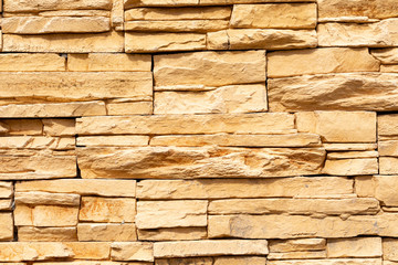 Texture of the yellow surface of a slate stone. Blocks of artificial finishing stone for wall decoration. Rough stone background