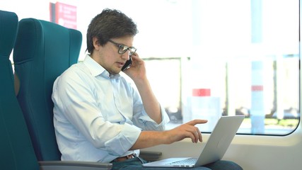 Young manager wearing a white shirt and jeans is riding a train to work and using his laptop