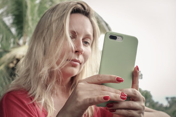 Adult blond woman holding , using and looking at iPhone 8 Plus