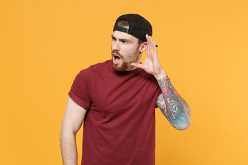 Shocked young bearded tattooed man guy in casual t-shirt, black cap posing isolated on yellow wall...