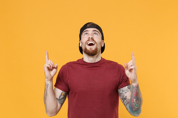 Excited young bearded tattooed man guy in casual t-shirt black cap posing isolated on yellow wall...