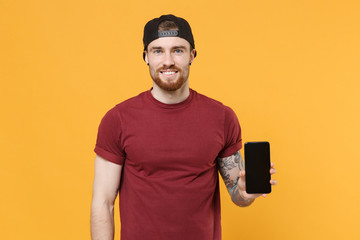 Smiling young bearded tattooed man guy in casual t-shirt black cap posing isolated on yellow...