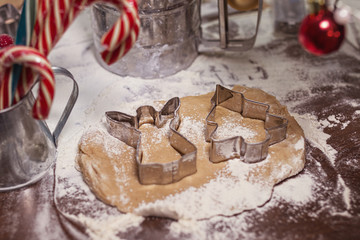 raw gingerbread brown spicy dough with metal shapes of angel and christmas tree on a wooden table with caramel cane and red christmas toys
