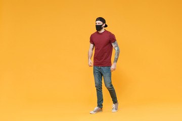 Fototapeta na wymiar Young tattooed man guy in casual t-shirt cap black face mask posing isolated on yellow wall background studio portrait. People sincere emotions lifestyle concept. Mock up copy space. Looking aside.