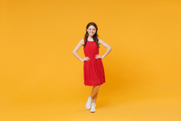 Smiling young brunette woman girl in red summer dress posing isolated on yellow wall background studio portrait. People emotions lifestyle concept. Mock up copy space. Stand with arms akimbo on waist.