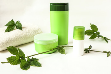 A set of skin care products and a white Terry towel among young green branches of hops, a place for the inscription.