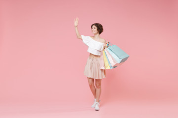 Smiling young woman in summer clothes hold package bag with purchases isolated on pink background. Shopping discount sale concept. Mock up copy space. Waving and greeting with hand as notices someone. © ViDi Studio