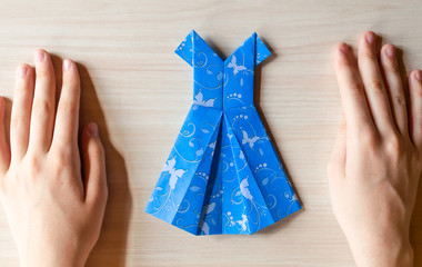 Girl's hands making origami blue dress from butterfly printed paper. Step by step instruction, step17. Mother's day, birhday, summer gift, family leisure time concept. DIY tutorial, flatlay, top view