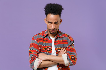 Dissatisfied young african american guy in casual colorful shirt posing isolated on violet background studio portrait. People emotions lifestyle concept. Mock up copy space. Holding hands crossed.