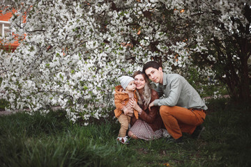 Beautiful young parents and their cute little son have fun near flowering trees