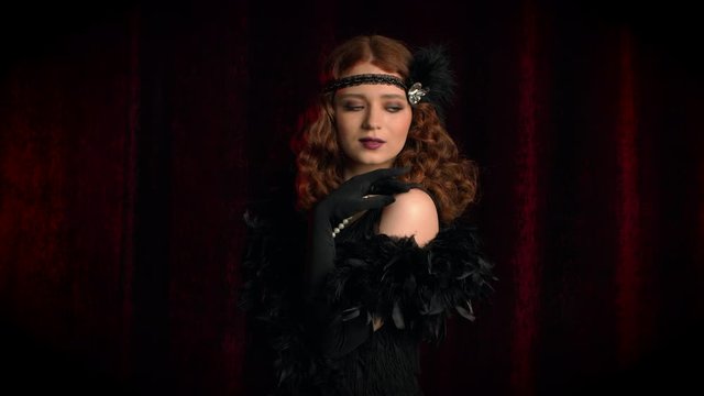 Old-fashioned sexy woman dressed in style of Flappers posing on dark background. Roaring twenties, retro, party, fashion concept