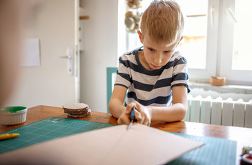 Naklejka premium Little boy cutting cardboard, quarantine project 