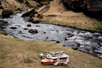 An impromptu wedding table for two on the shores of mountain, on the grass in Iceland. A table of construction pallet decorated with driftwood and omits. It has plates, glasses, candles and guitar