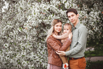 Happy parents mom and dad, son stand in the garden in spring against the background of flowering trees