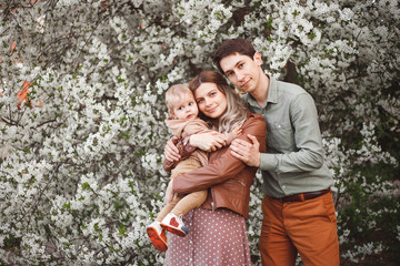 Beautiful young parents and their cute little son have fun near flowering trees