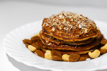 Healthy breakfast, close-up of homemade american vegan pancakes with raw cashew and almond nuts in white plate.