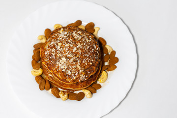 Healthy breakfast, top view of homemade american vegan pancakes with raw cashew and almond nuts in white plate.