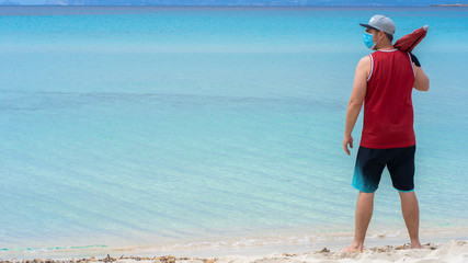 man with umbrella and mask on the beach in front of turquoise sea