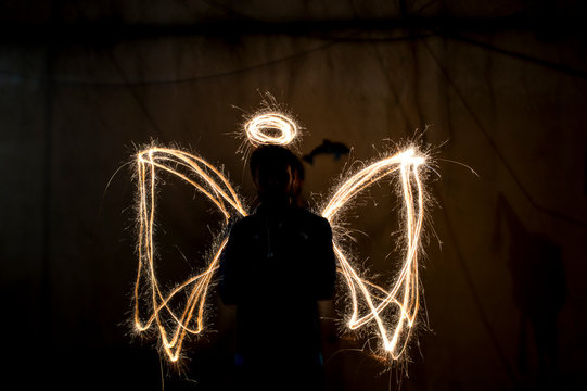 Silhouette Man Standing Against Lighting Painting Making Angel Wings And Halo In Dark