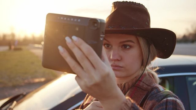Portrait beautiful young lady wearing cowboy hat using instant camera like mirror fixing her face ready to take polaroid pictures. Country landscape. Sunsets.