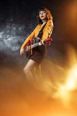 Pretty young hipster woman with curly hair with red guitar in neon lights. Rock musician is playing...