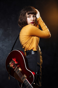 Serious young hipster woman with curly hair with red guitar in neon lights. Rock musician is playing electrical guitar.