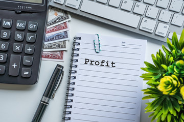 Profit text with notepad, paper clip, keyboard, decorative flower, fountain pen, calculator and banknotes currency on white background. Business and Copy space concept.