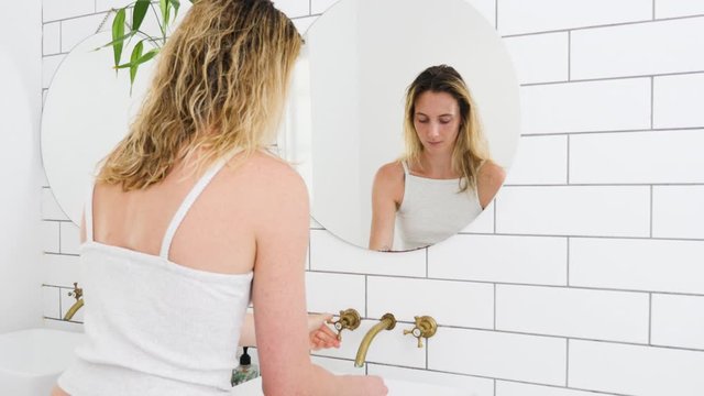  Beautiful woman brushing teeth and looking in the mirror in the bathroom