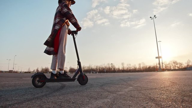 Cool active girl in cowboy hat enjoying ride electric gyro scooter at abandoned parking space. Sunset landscape. Mobile transportation. Ecology concept.