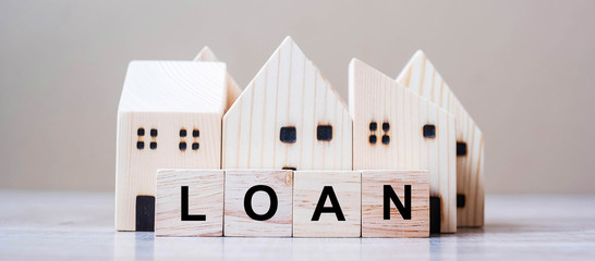 LOAN cube blocks with wooden house model on table background. fall Business, investment, Crisis,...